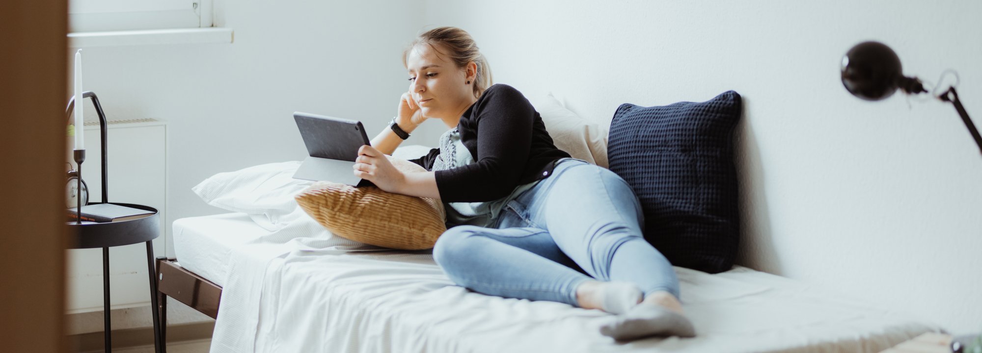 Junge Frau, die auf dem Bett liegt und auf den Bildschirm eines Tablets blickt.